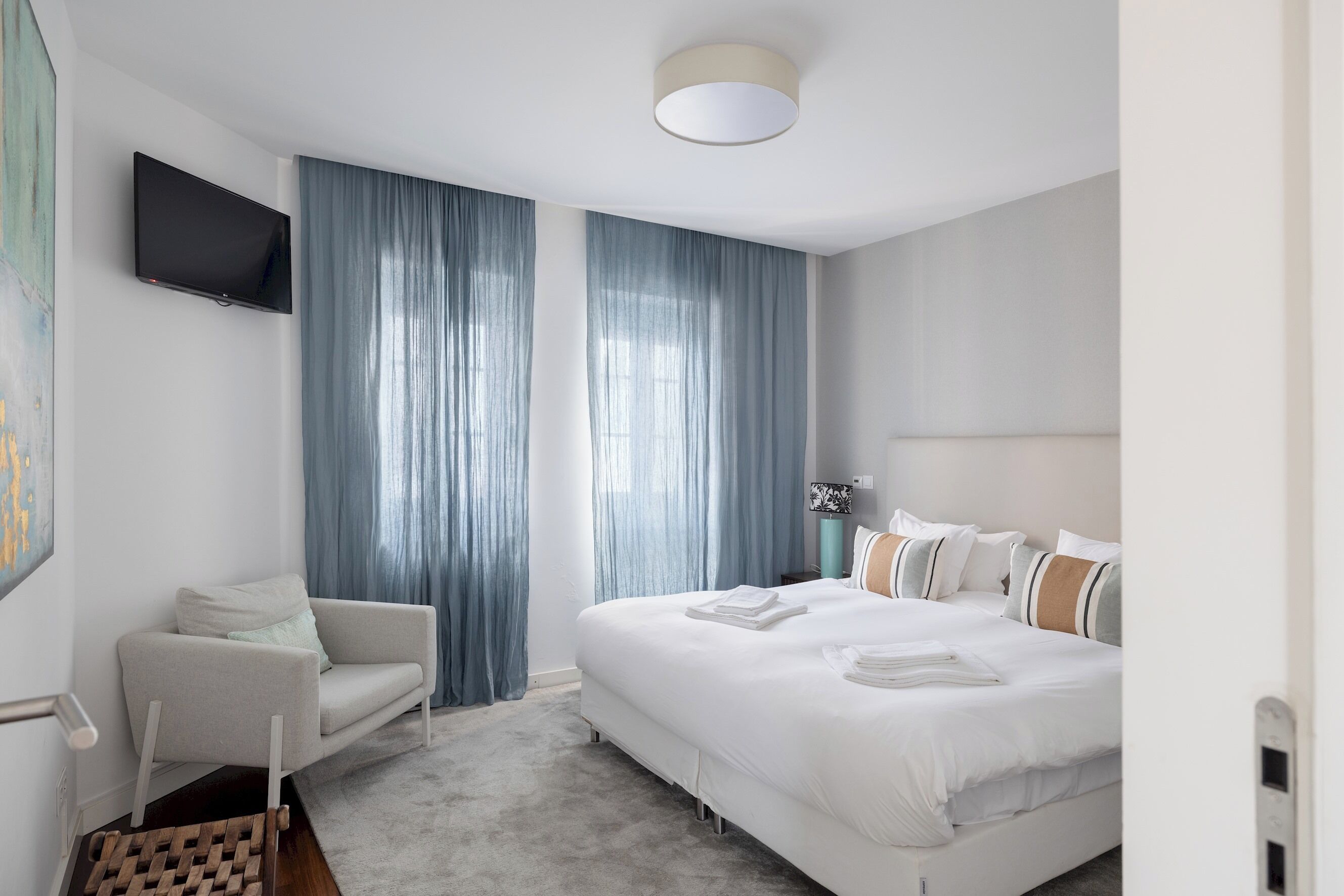 A modern hotel room with a large bed, a seating area, and a flat-screen TV mounted on the wall.