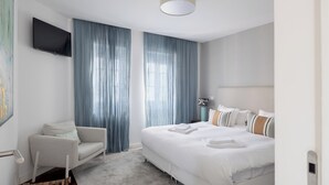 Une chambre d’hôtel moderne dotée d’un grand lit, d’un coin salon et d’un téléviseur à écran plat fixé au mur.