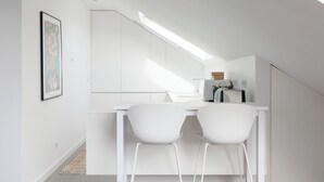 Une cuisine moderne avec des meubles blancs, une lucarne et deux chaises blanches autour d’une table blanche.