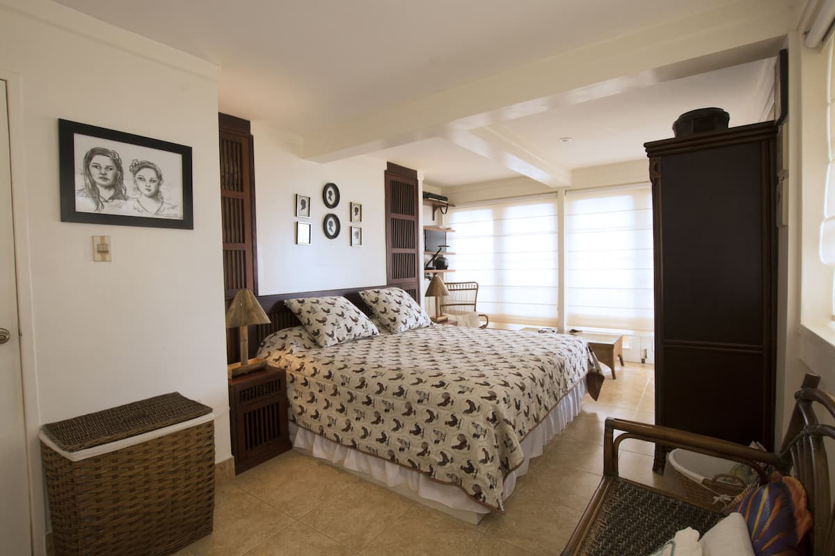 A bedroom with a bed, bedside tables, a lamp, a chair, a wardrobe, and a window.