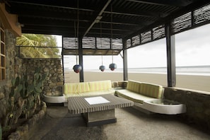 Un espace extérieur abrité, avec un mur en pierre, une table en béton et une vue sur la plage.