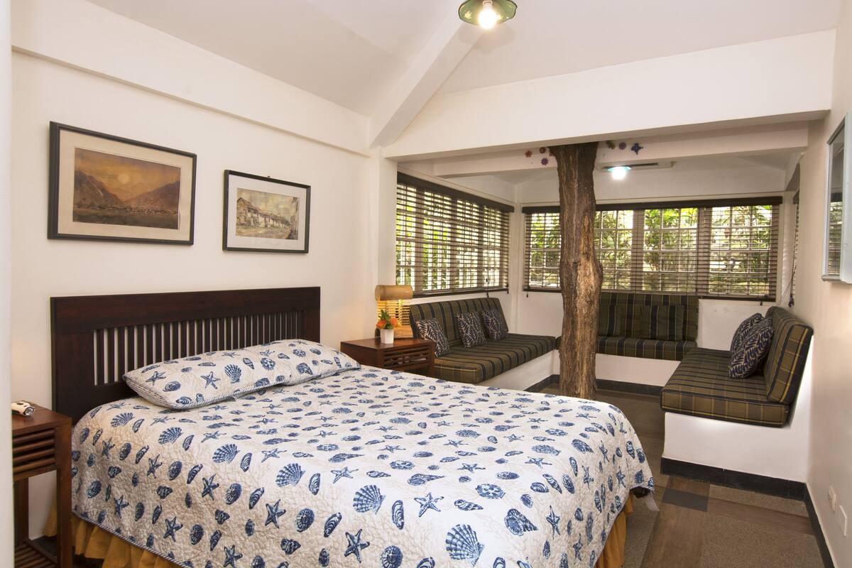 A bedroom with a bed, a sofa, and a window with blinds.