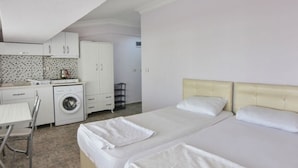 Ett hotellrum med två sängar, en tvättmaskin, ett matbord och ett litet kök.