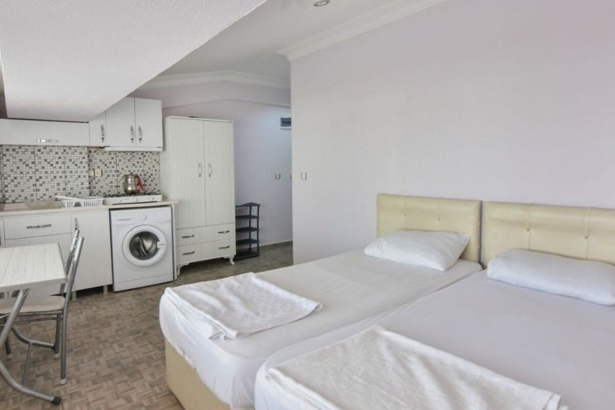 Ein Hotelzimmer mit zwei Betten, einer Waschmaschine, einem Esstisch und einer Küchenzeile.