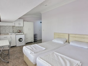 Ein Hotelzimmer mit zwei Betten, einer Waschmaschine, einem Esstisch und einer Küchenzeile.