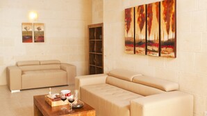 A living room with a wooden coffee table, beige sofas, a hanging light fixture, and a painting on the wall. - Serkuzan (Xaghra)