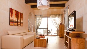 A living room with a sofa, coffee table, wooden cabinet, and artwork on the wall. - Serkuzan (Xaghra)