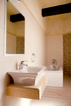 A bathroom with a white sink, a mirror, and a bathtub. - Serkuzan (Xaghra)