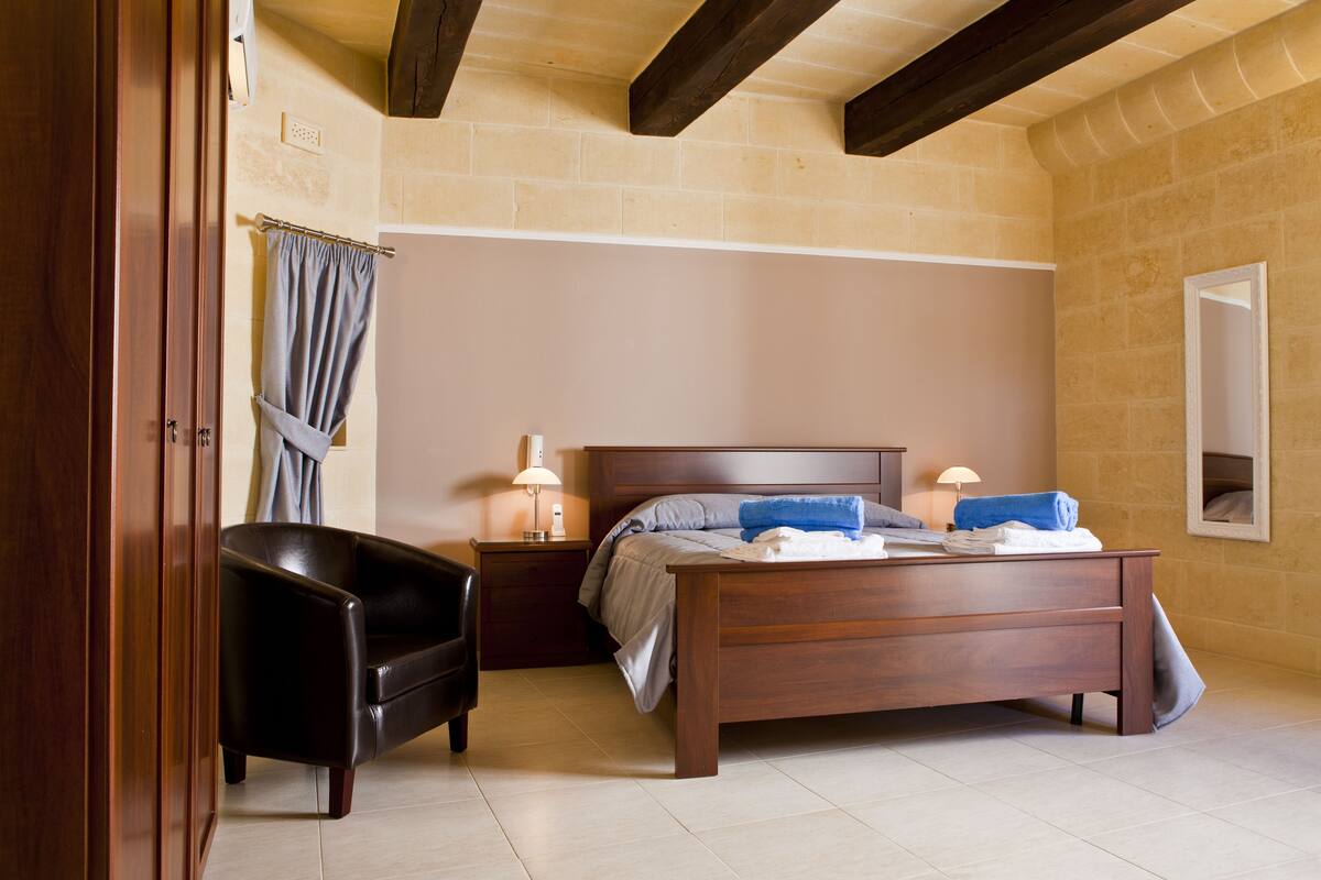 Un dormitorio con una cama de madera, una mesita de noche, una lámpara, una silla y un espejo en la pared.