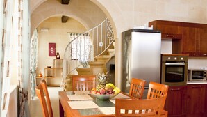 A dining area with a wooden table and chairs, a refrigerator, an oven, and a staircase leading to an upper level. - Serkuzan (Xaghra)