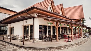 A building with a covered patio area, outdoor seating with tables and chairs, and hanging flower baskets. - Pension Zwicker (Lubotice)
