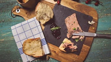 Une planche à découper en bois, avec des tranches de pain, un couteau et un morceau de viande recouvert d’une pâte sombre.