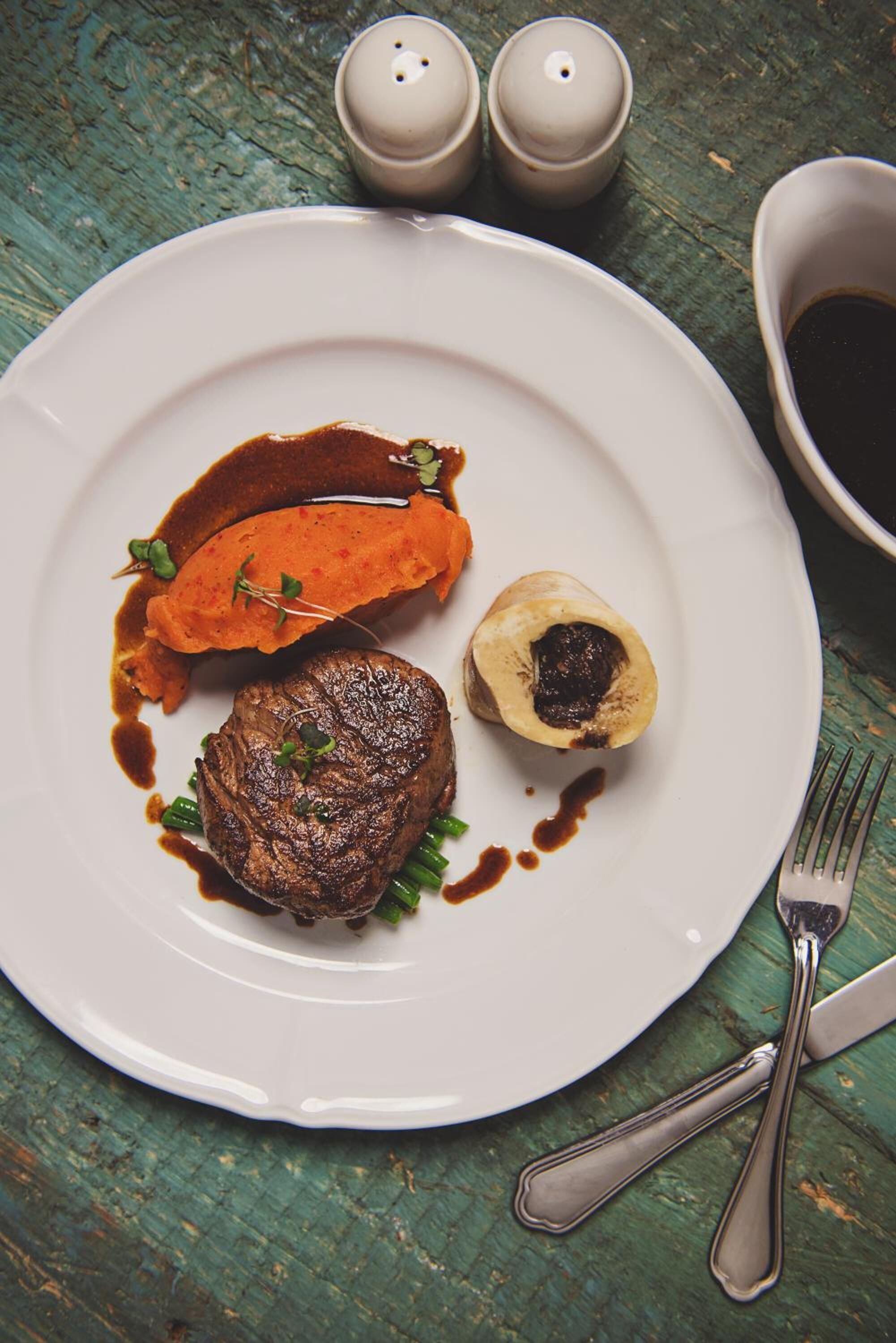 A plate with a steak, a baked sweet potato, and a baked potato topped with a pat of butter, served on a white plate.
