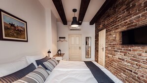 A bedroom with a large bed, a brick wall, a mounted TV, and a door. - Pension Zwicker (Lubotice)
