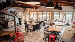 A restaurant with a mix of wooden and metal furniture, large windows, and a patterned floor. - Pension Zwicker (Lubotice)