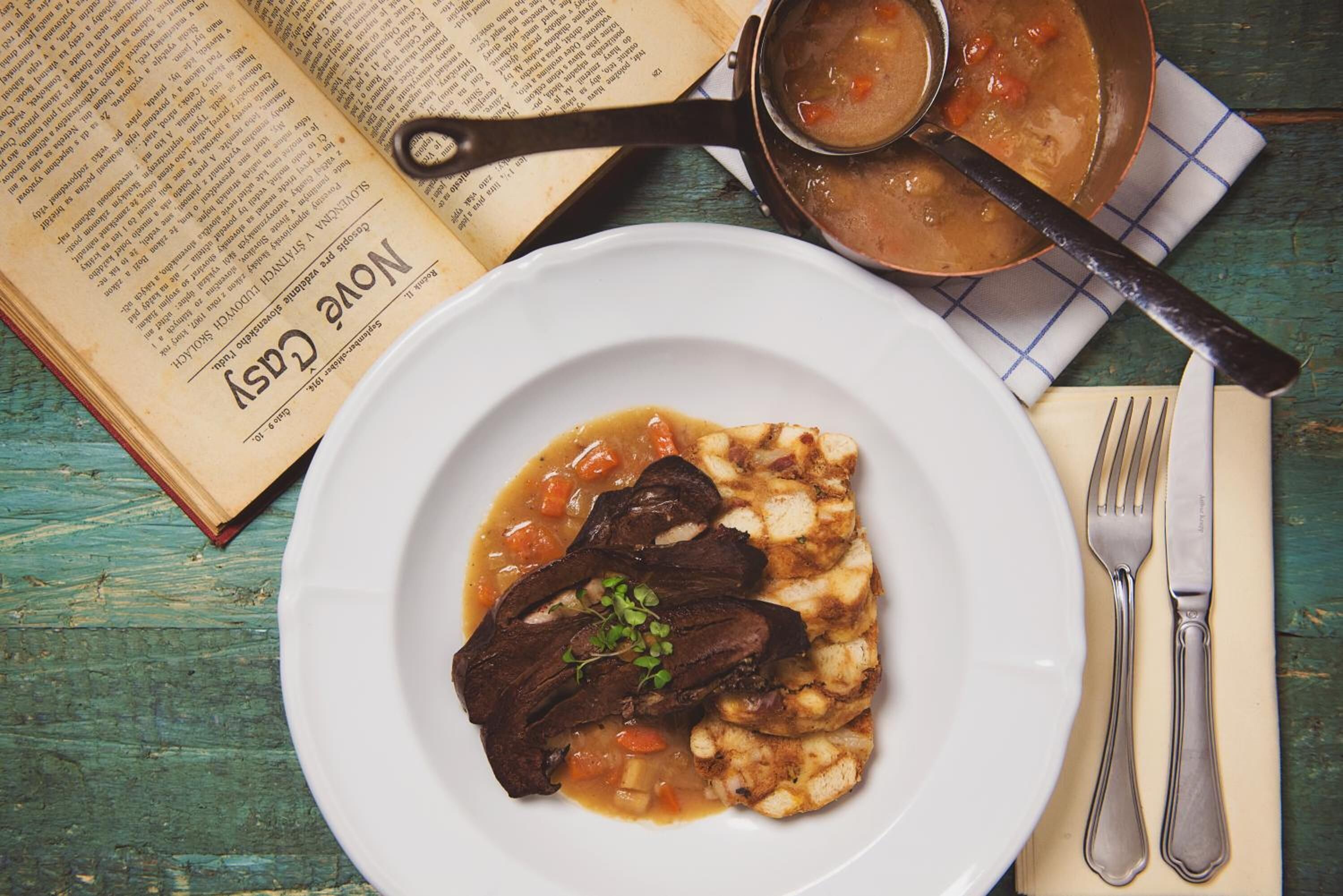 Un plato de comida, con un libro y una olla al fondo.