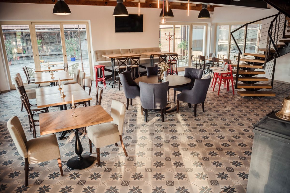 A restaurant with multiple dining tables and chairs, a staircase, and large windows.