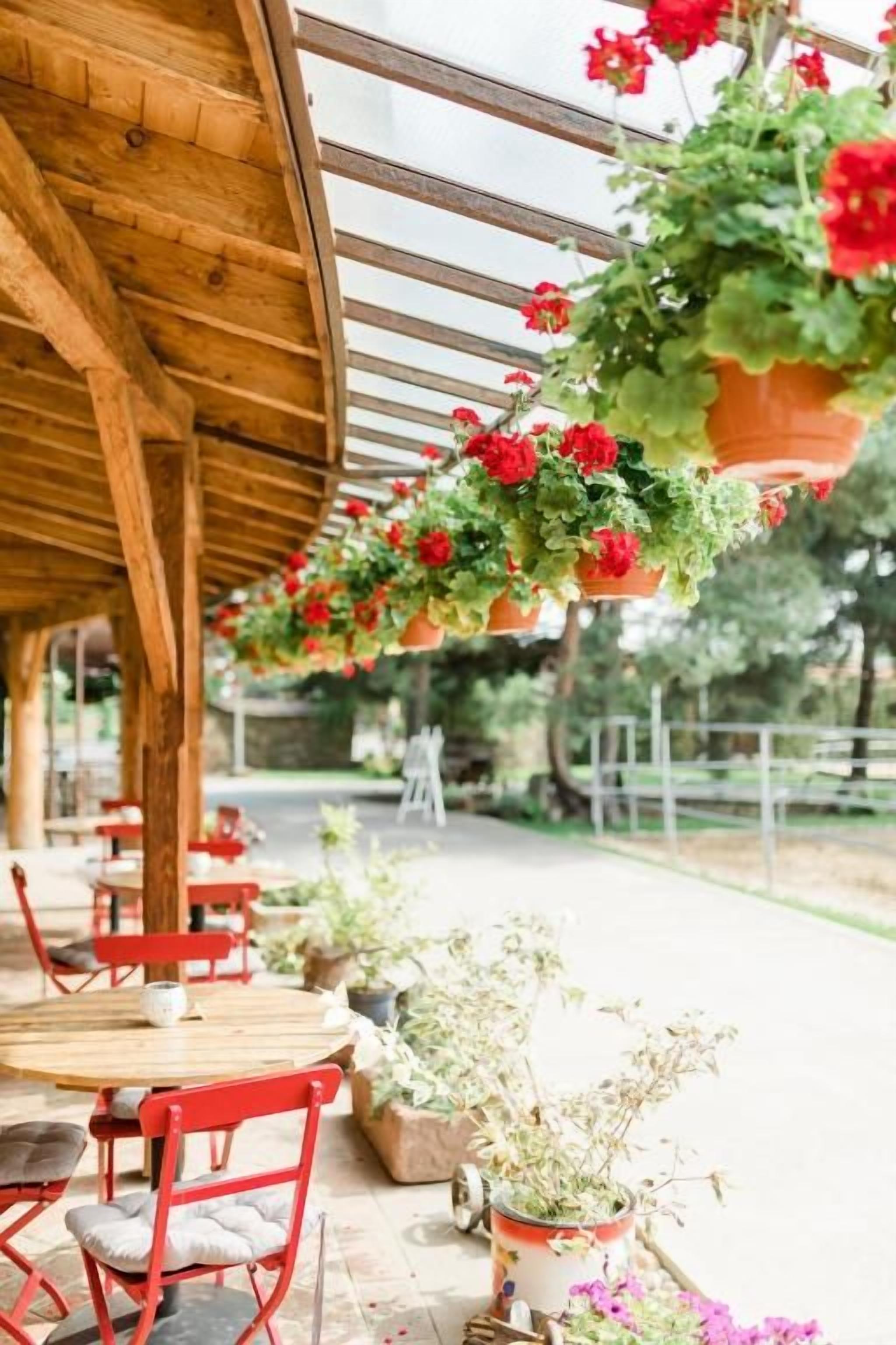 An outdoor seating area with wooden tables and chairs, potted plants, and hanging flower baskets.