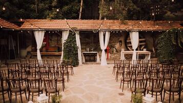 An outdoor event space with stone flooring, wooden chairs, and tables arranged for an event.