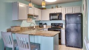 A kitchen with white cabinets, a granite countertop, a black refrigerator, and a dining area with white chairs. - Fantastic Beach location! With Ocean View.1 Bedroom, Bunk beds, Sofa bed 1 bath. (Destin)