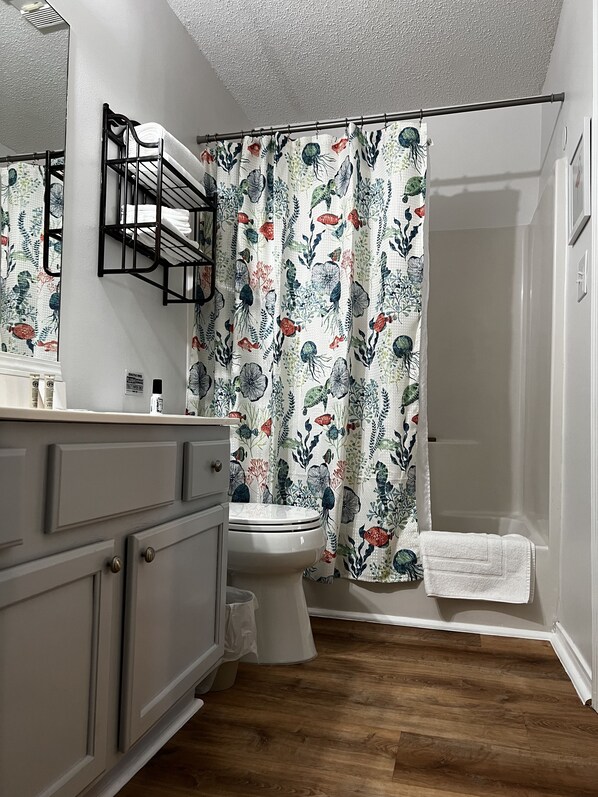 Casa de banho com cortina de chuveiro estampada com padrão floral, sanita, lavatório com toalha e espelho.