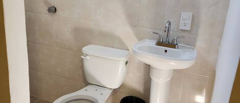 Un baño con inodoro, lavamanos y un cubo de basura.