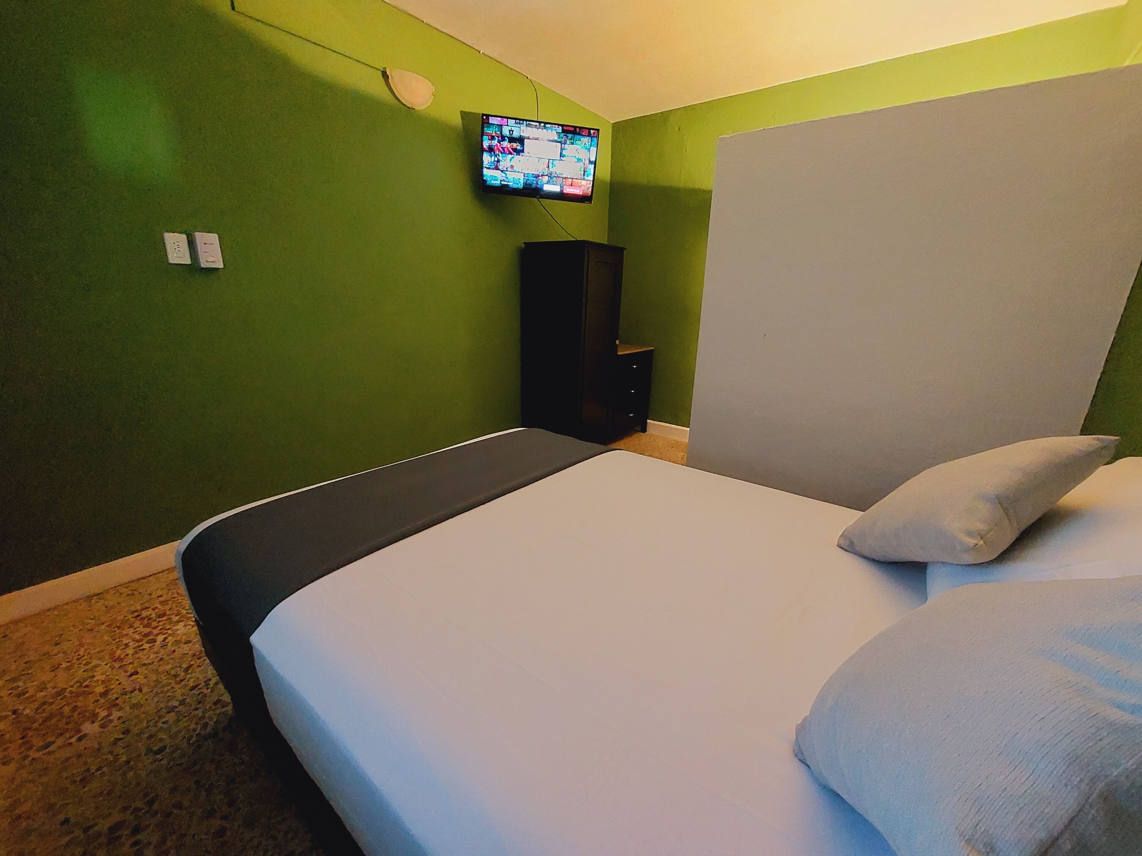 A hotel room with a bed, a television mounted on the wall, and a small cabinet.