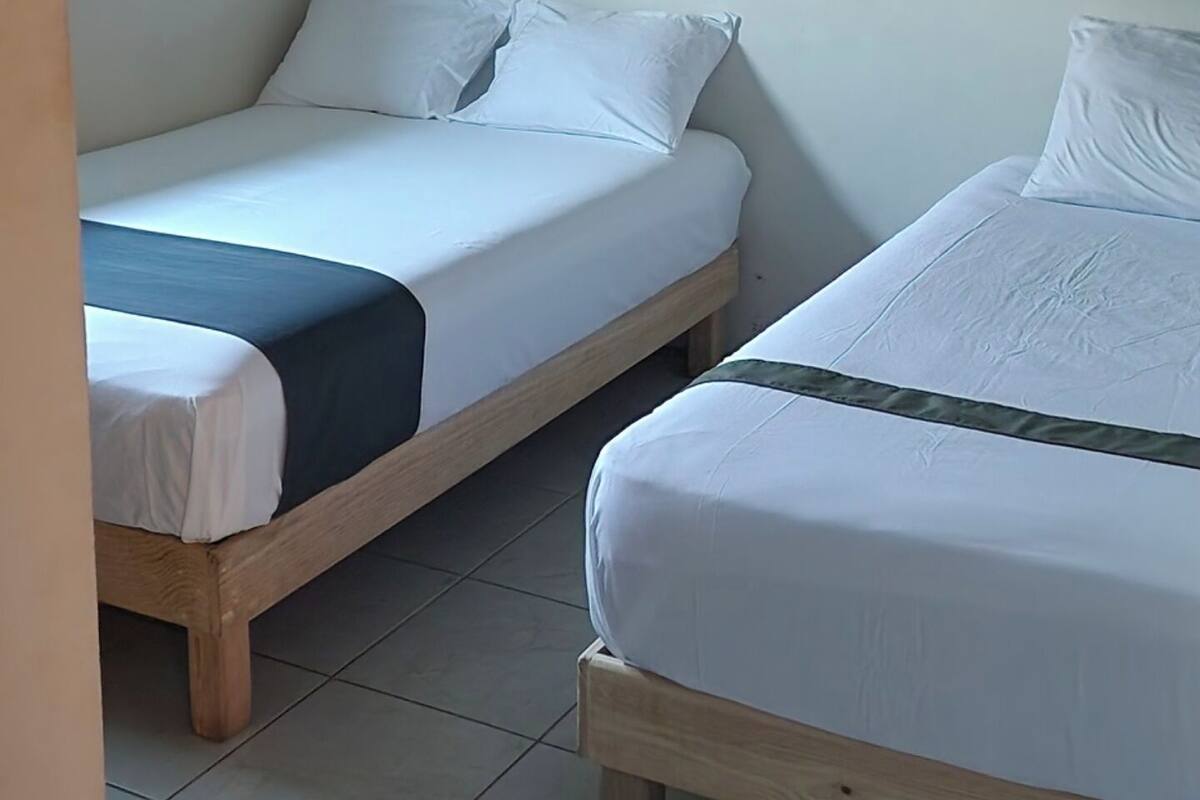 Une chambre avec deux lits simples, chacun doté de draps blancs et d’un cadre en bois.