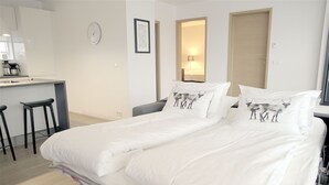 A hotel room with a bed, two white pillows with animal prints, a desk with a kettle, and a chair. - Óm Apartments (Reykjavik)