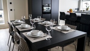 A modern dining area with a long table set for six, black chairs, and a kitchen in the background. - Óm Apartments (Reykjavik)