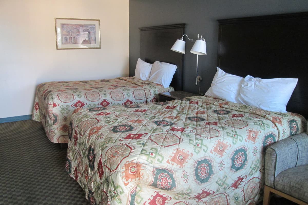 A hotel room with two beds, a nightstand, a chair, a framed picture on the wall, and two bedside lamps.