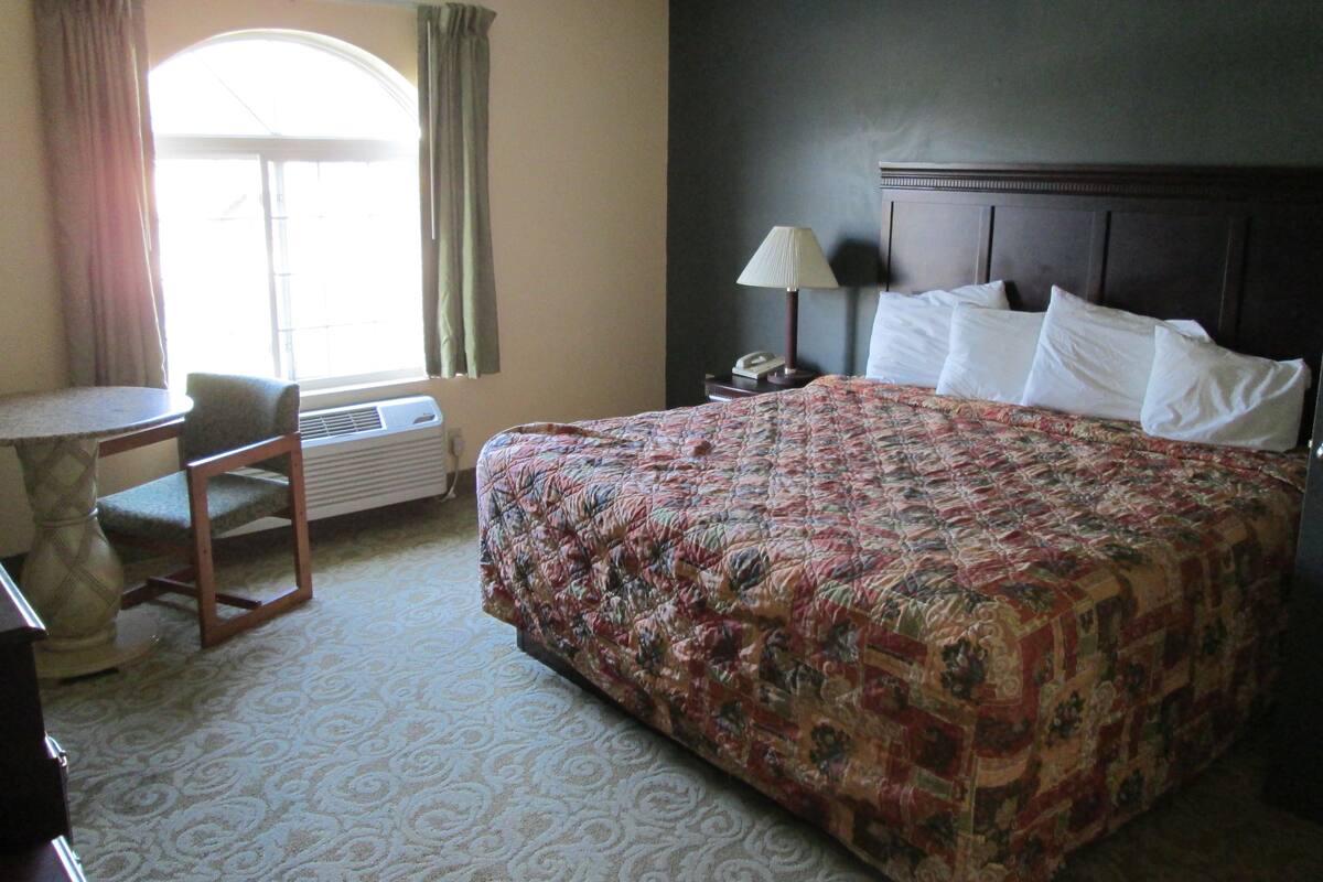 A hotel room with a large bed, a desk, a chair, a lamp, and a window with curtains.