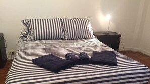 A bed with striped bedding, two pillows, a bedside lamp, and rolled towels on the bed. - Incredible Rodriguez Pena (Buenos Aires)