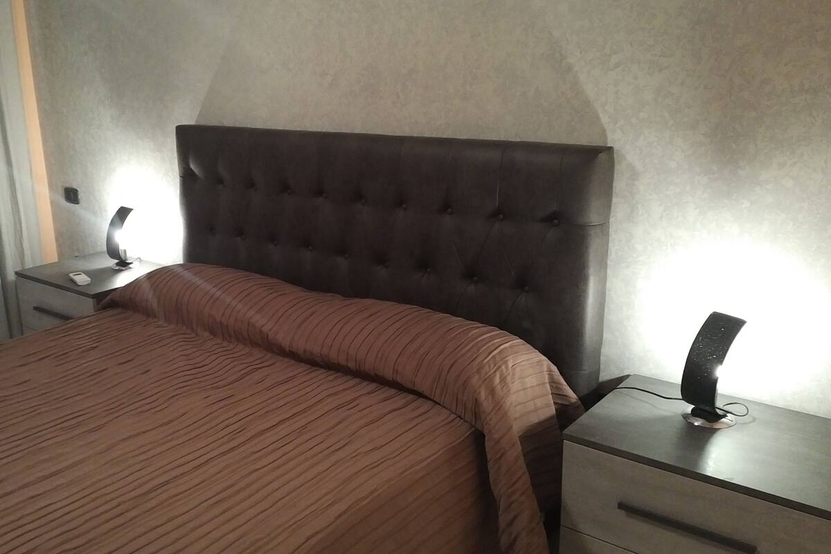 Ein Hotelzimmer mit einem großen Bett, einem Nachttisch mit einer Lampe und einem Beistelltisch mit einem Telefon.