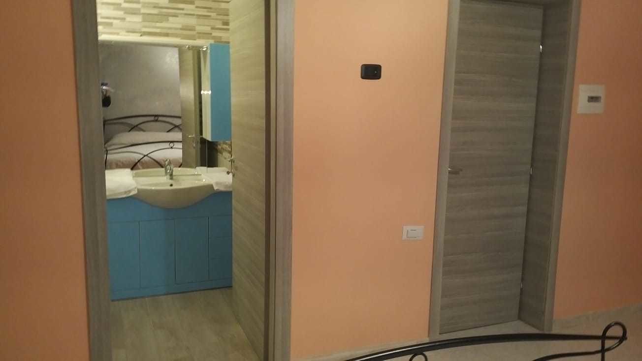 A hotel room with a bathroom featuring a sink and mirror, a door, and a visible electrical cord.