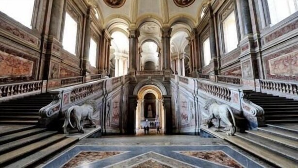Un magnifique escalier, orné de balustrades travaillées et doté d’un sol en marbre, mène à un espace central où se trouve une statue.