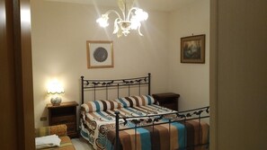 Ein Schlafzimmer mit Metallbettgestell, gestreifter Bettwäsche, einem Chandelier, einem gerahmten Bild an der Wand und einer Nachttischlampe.