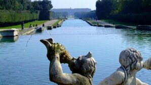 Un canal bordé de statues, un pont en arrière-plan et des personnes se promenant le long du sentier.