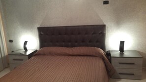 Ein Schlafzimmer mit einer gepolsterten Kopfstütze, einer braun gestreiften Bettdecke und zwei Nachttischen mit Lampen.