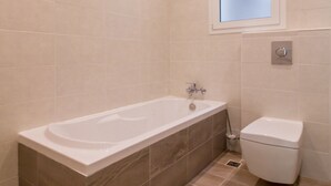 A bathroom with a bathtub, toilet, and a window. - Ocean Gardens B3 (Naxxar)