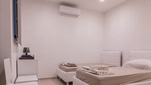 A modern bedroom with a bed, a chair, a bedside table, and an air conditioning unit. - Ocean Gardens B3 (Naxxar)