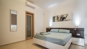 A modern bedroom with a bed, bedside tables, a door, and a wall-mounted air conditioner. - Ocean Gardens B3 (Naxxar)