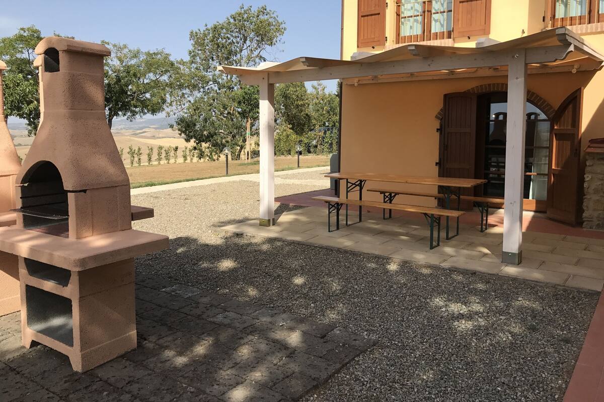 An outdoor patio with a stone oven, a covered seating area, and a view of the countryside.