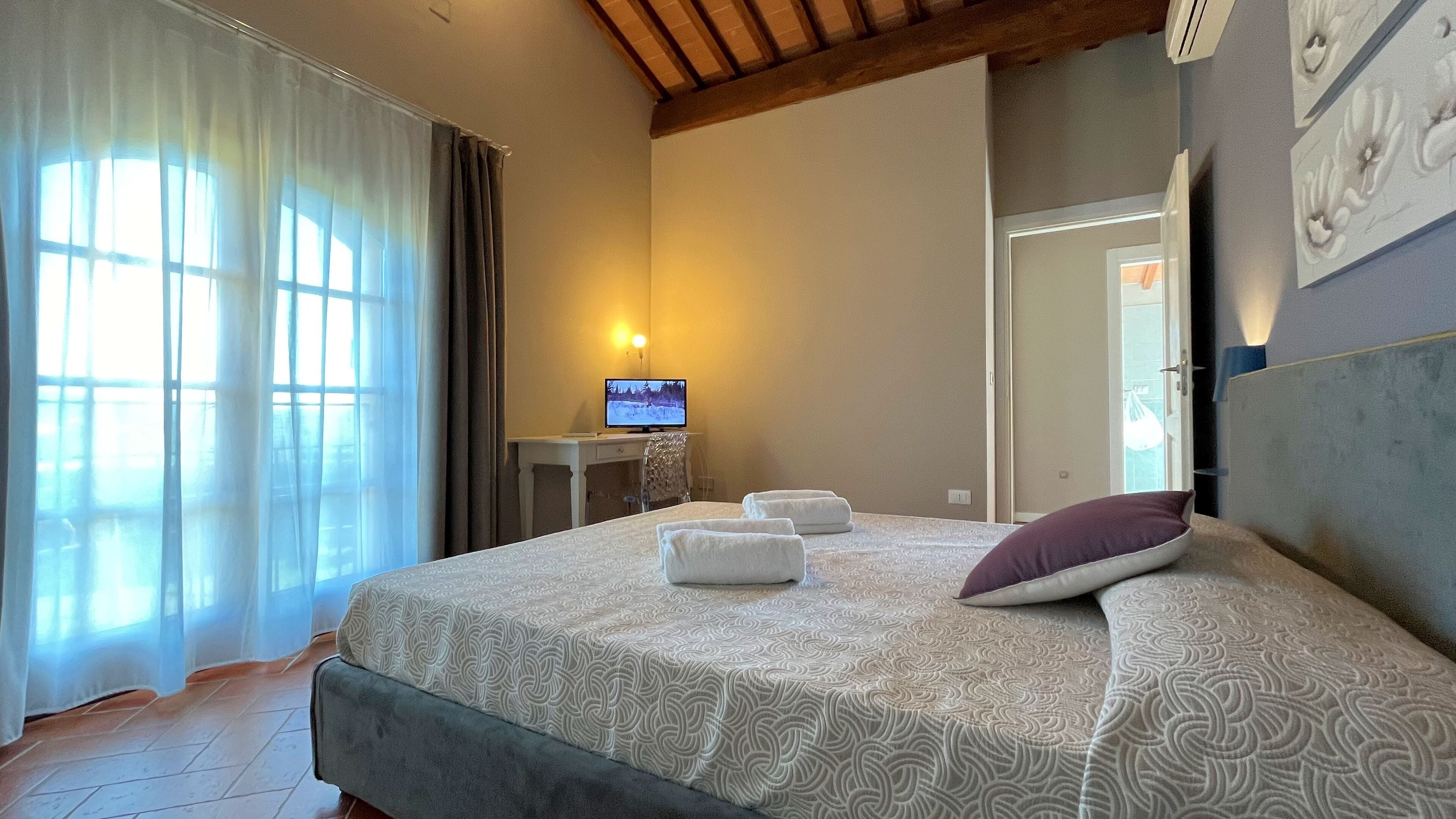 Une chambre d’hôtel avec un lit, un bureau avec un ordinateur, une fenêtre avec des rideaux et un miroir au mur.