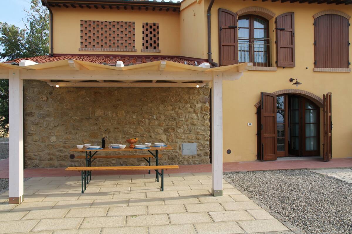 A covered outdoor dining area with a stone wall backdrop, a wooden table, and benches.