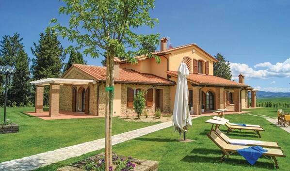 A two-story house with a stone facade, a tiled roof, and a garden with lawn chairs and an umbrella. - Borgo del Silenzio (Lajatico)