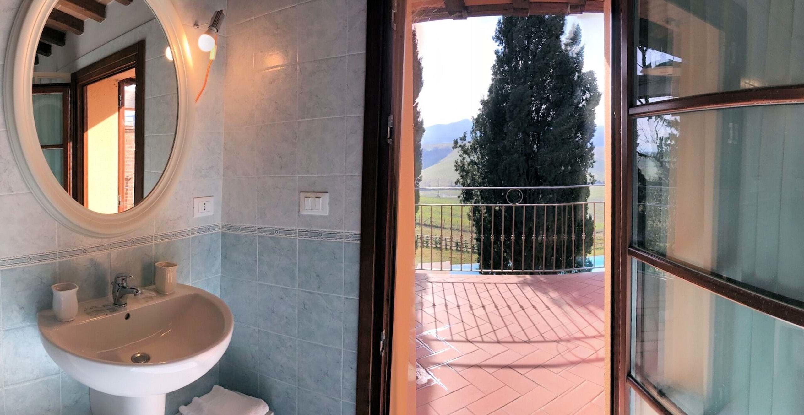 A bathroom with a sink, mirror, and a view of a balcony with a railing and a tree.