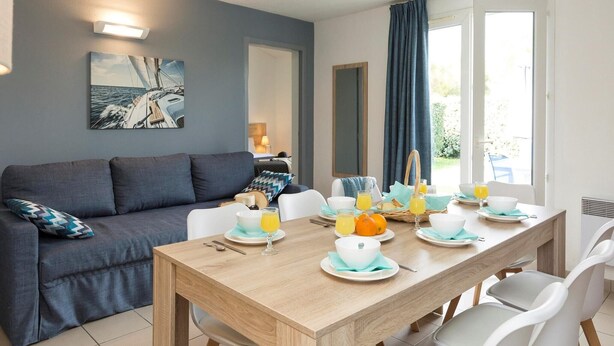 Ein zeitgemäßer Essbereich mit einem Holztisch, der für das Frühstück gedeckt ist, einer grauen Couch und Blick ins Freie.