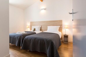 A hotel room with two beds, each with a patterned bedspread, a wooden headboard, bedside lamps, and a small table with a lamp.