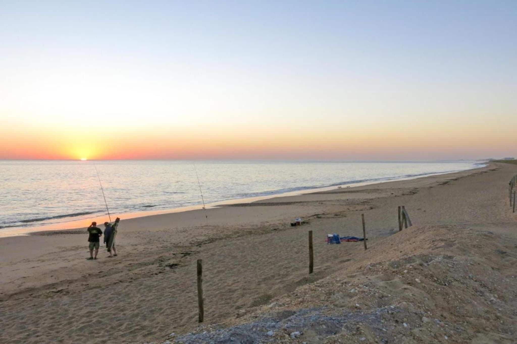 Ein Strand bei Sonnenuntergang, ein sandiger Uferstreifen und einige Angler.